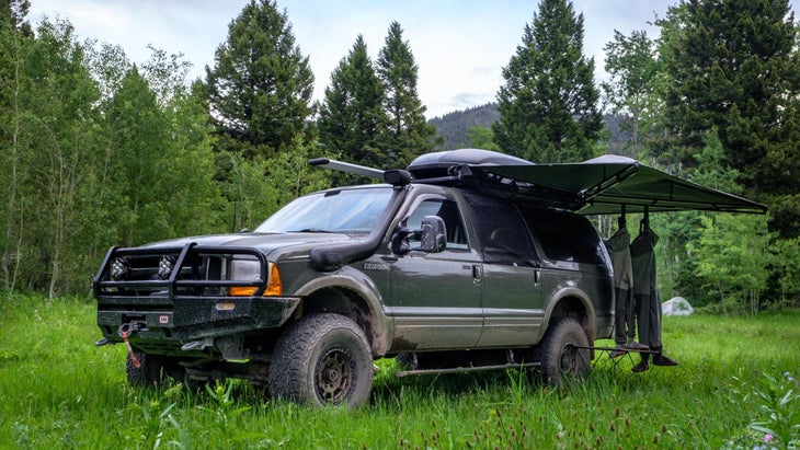 Ford Excursion pickup truck decked out with awning and gear parked in grassy field