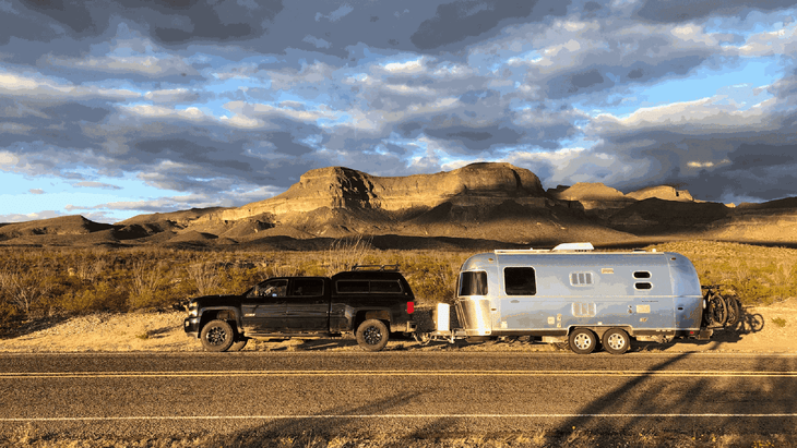 Pickup truck towing an Airstream trailer parked on side of road in desert. 